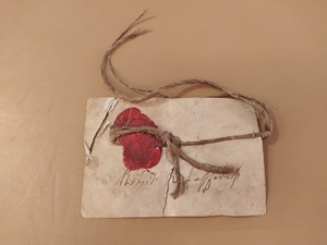Old paper tag with twine and red wax seal attached, lying on leather surface