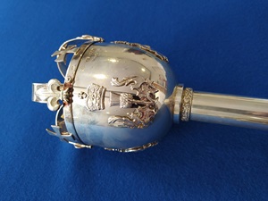 Polished silver mace with fleur-de-lis and crosses decoration lying on blue material surface.