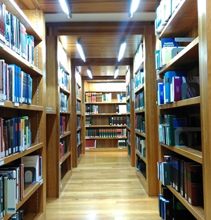 View along a library corridor, with wooden shelves and floors and books on shelves on either side.